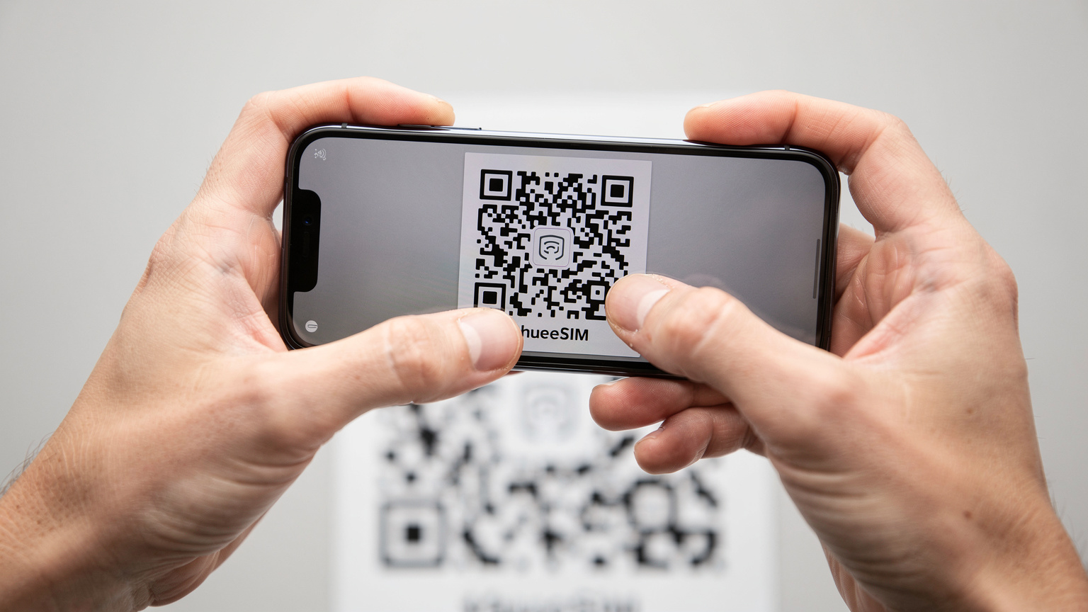 Un primo piano di mani che tengono uno smartphone, mostrando il processo di scansione di un codice QR per attivare un'eSIM su uno sfondo neutro e luminoso, mettendo in risalto l'interazione umana con la tecnologia.