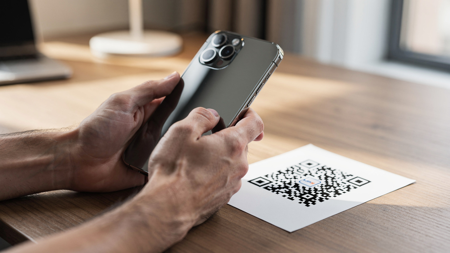 Detailní záběr rukou muže, který na iPhonu 18 Pro Max skenuje QR kód pro aktivaci eSIM, s rozmazaným pozadím stolu.
