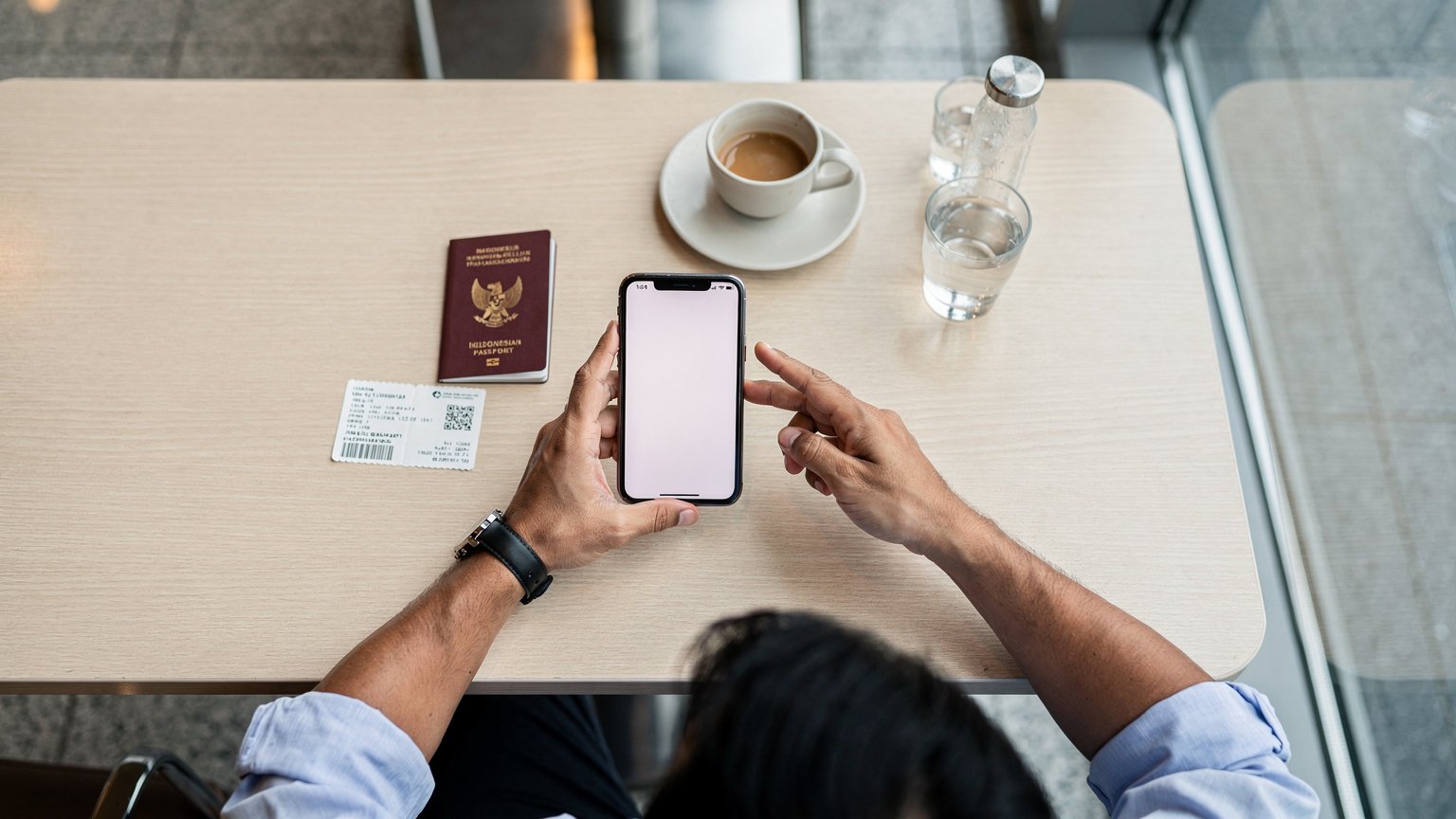Seorang pria paruh baya Indonesia sedang dengan saksama membandingkan paket eSIM di layar ponselnya, dengan paspor dan tiket pesawat di atas meja di sebuah kafe bandara yang tenang.