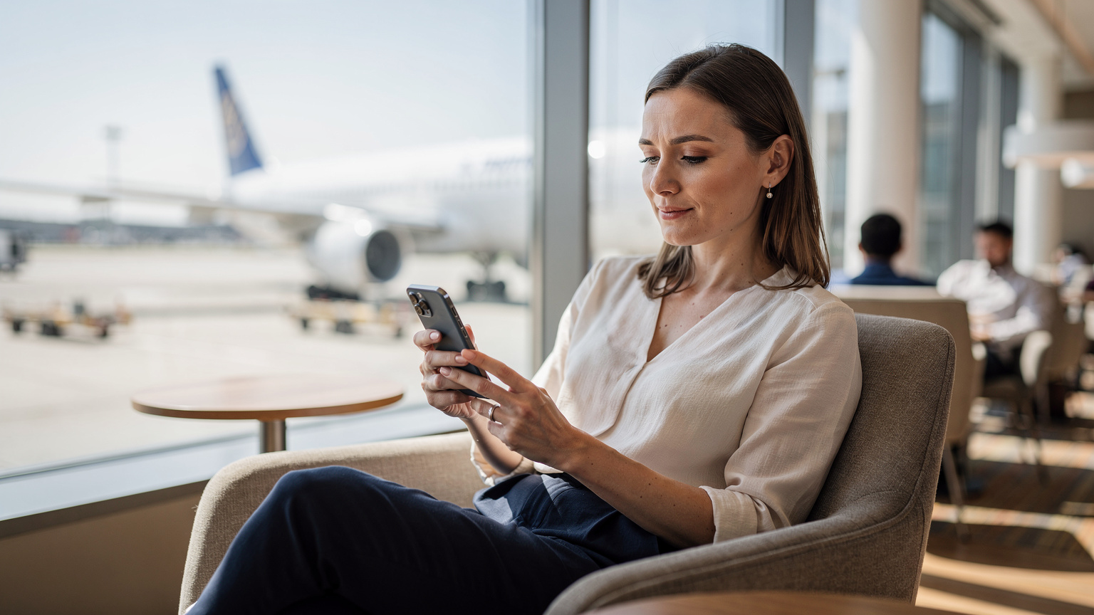 A woman in a stylish airport lounge, looking relaxed while setting up her Cellesim eSIM on her smartphone, with a large window showing an airplane outside.