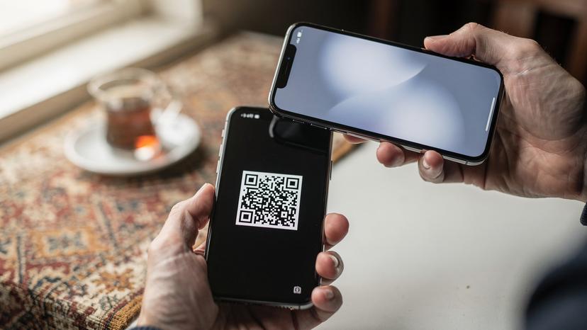 O mână apropiată a unei persoane scanează un cod QR de pe ecranul unui alt smartphone, demonstrând procesul rapid de activare a unui eSIM, cu o notificare de succes vizibilă pe ecranul receptor.