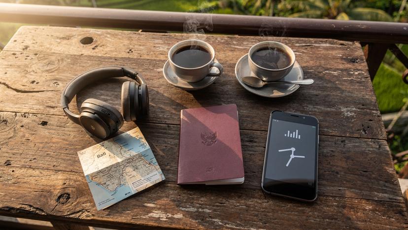 An overhead flat-lay shot of travel essentials, including a passport, smartphone with an active eSIM, headphones, and a local Indonesian map, ready for adventure.