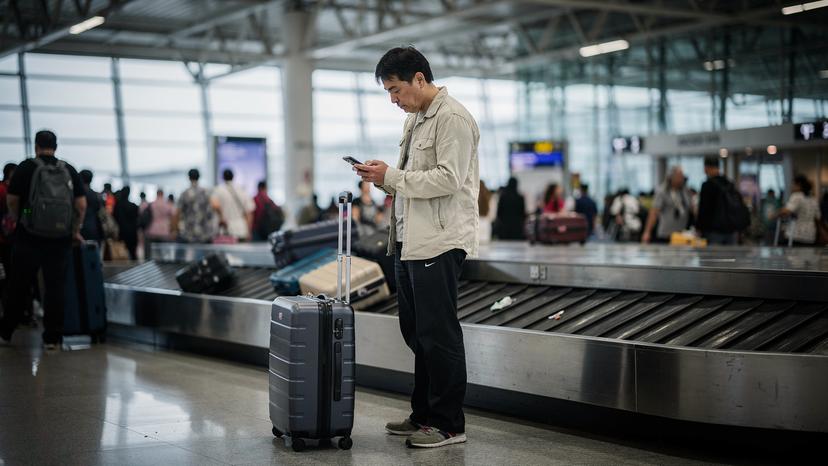 バンコクのスワンナプーム空港に到着した旅行者が、手荷物を持って到着ロビーでスマートフォンを確認する様子