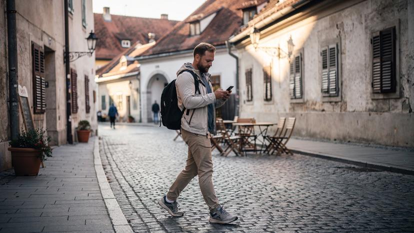 Ein Reisender nutzt sein Smartphone für die Navigation in einer ruhigen Fußgängerzone in Maribor, Slowenien, mit einem historischen Gebäude im Hintergrund.