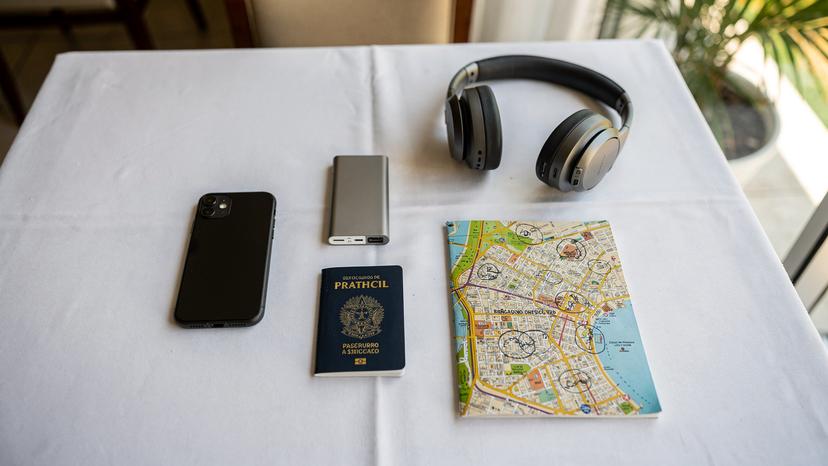Uma mesa de café da manhã em um hotel em Salvador, com um iPhone 11, um power bank, passaporte, fones de ouvido e um mapa da cidade, tudo organizado para um dia de turismo.