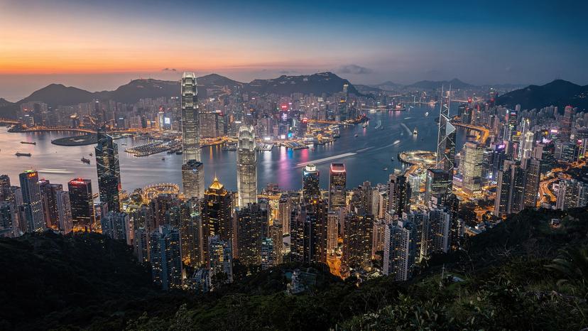 Pandangan udara dari Victoria Peak di Hong Kong, menampilkan cakrawala kota yang ikonik di bawah langit senja, dengan kapal-kapal kecil di Pelabuhan Victoria.